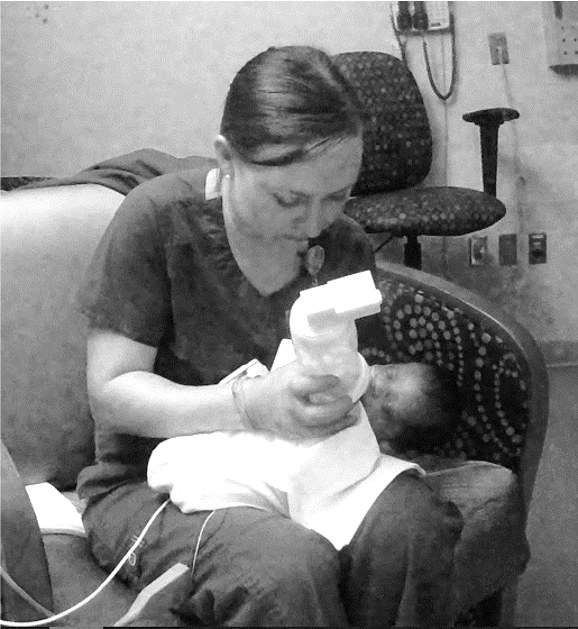 A nurse in a hospital chair feeding a baby with the instrumented feeding bottle