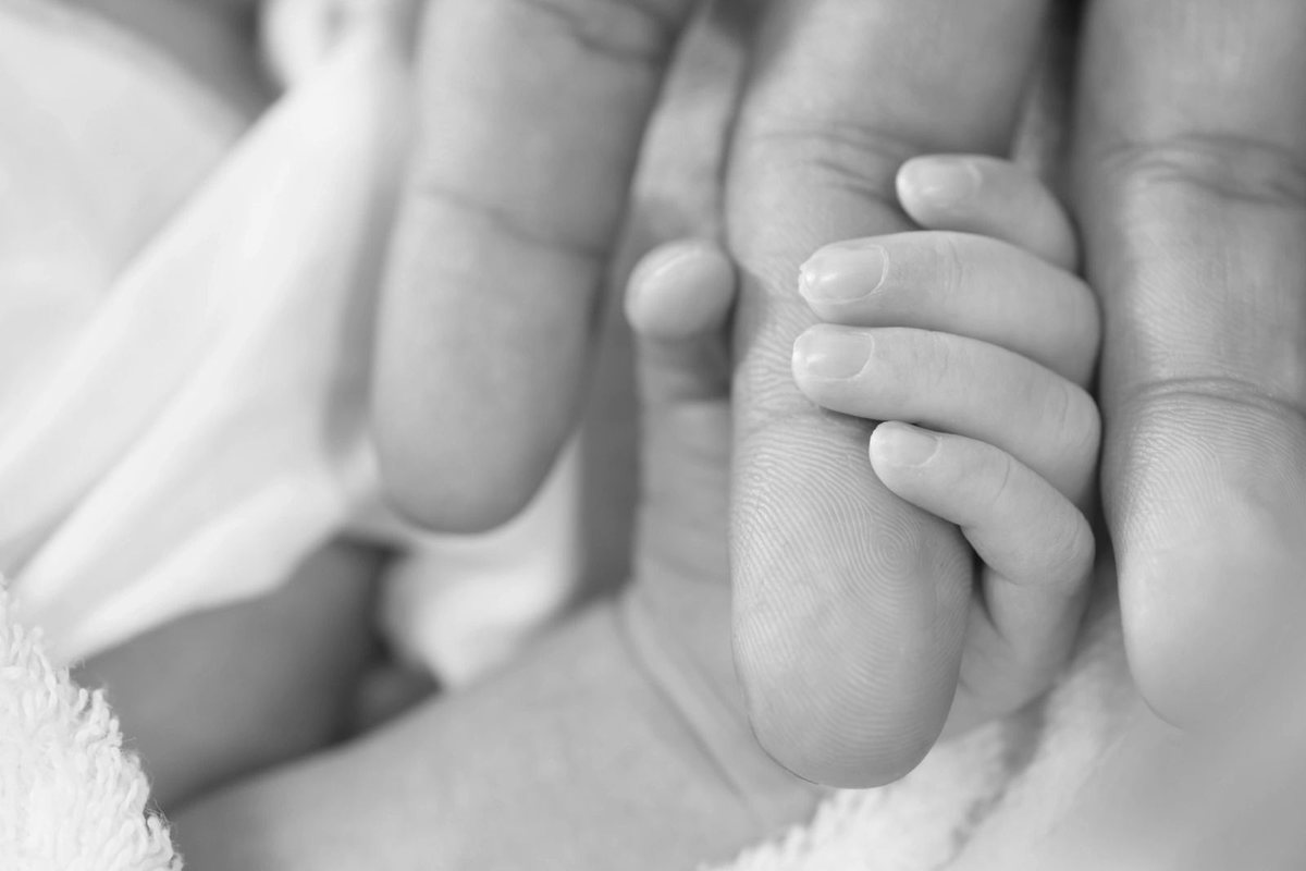 A newborn’s hand holding an adult’s finger